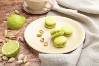 Green macarons or macaroons cakes with cup of coffee on a brown concrete background and linen