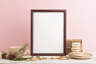 Brown wooden frame mockup with cup of coffee, almonds and macaroons on pink pastel background.