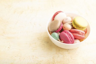 Multicolored macaroons and chocolate eggs in ceramic bowl on beige concrete background. side view,