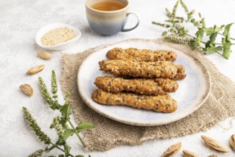 Crumble cookies with seasme and almonds on ceramic plate with cup of green tea and linen textile on