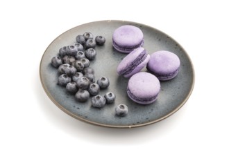 Purple macarons or macaroons cakes with blueberries on ceramic plate isolated on white background.