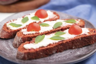 Red beet bread sandwiches with cream cheese and tomatoes on white concrete background and blue