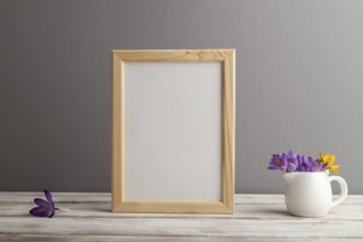 Beige wooden frame mockup with snowdrop crocus flowers on gray paper background. Blank, vertical