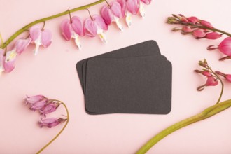 Black business card with pink dicentra, broken heart flowers on pink pastel background. top view,