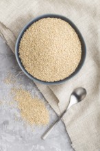 Blue ceramic bowl with raw white quinoa seeds on a gray concrete background and linen textile. Top