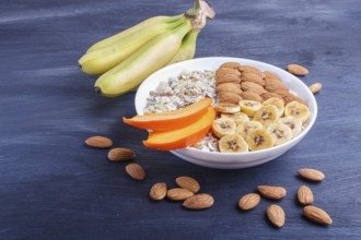 A plate with muesli, almonds, banana, sliced persimmon on a black wooden background. close up. copy