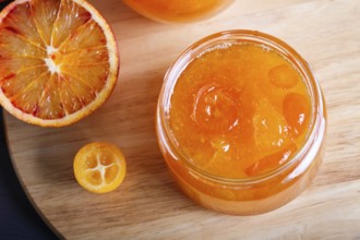 Orange and kumquat jam in a glass jar with fresh fruits on a wooden kitchen board. Homemade, close