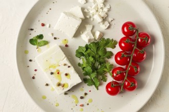 Feta cheese, for salads, with cherry, green butter, greens, on a white plate, appetizer, top view,