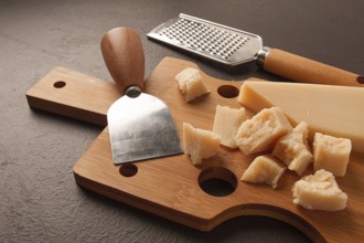 Hard cheese, parmesan, on a cutting board, cheese knife, grater, top view, no people