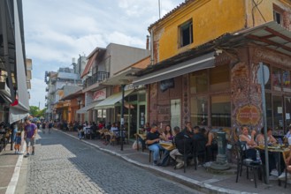 People enjoying food and drinks in outdoor seating along a lively street, Alexandroupoli,