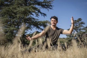 A middle-aged Caucasian man practices Kung Fu on a hill, performing stretching, balancing, and