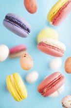 Multicolored flying macaroons and chocolate eggs frozen in the air on blurred blue background. top