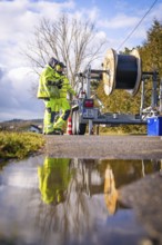 Worker inspecting a cable drum next to a reflective pool of water, fibre optic construction,