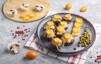 Stuffed fried champignons with cheese, kumquats and green peas on a gray concrete background.