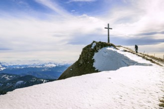 A hiker walks to the Hochgern summit cross over a snow-covered ridge, in the Chiemgau Alps in