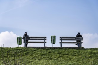 Benches on a dyke on the Weser in Bremerhaven, two people sitting symmetrically away from each