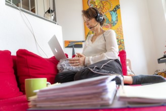 Woman, mid-50s, works from home, with laptop and communicates with colleagues via headset, home