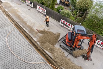 Construction workers lay fibre optic cable in trench under asphalt, cable trench, excavator,