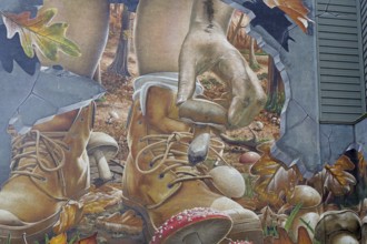 A mural shows a hand picking up a mushroom next to a boot in an autumnal forest, Mural Trail,