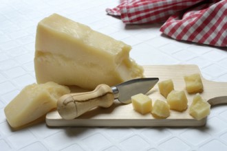 A piece of Parmesan cheese and chopped pieces of cheese on a wooden board