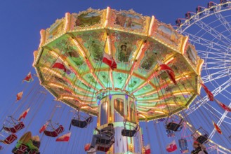 Illuminated carousel and Ferris wheel at night in a lively amusement park, funfair, wave flight,