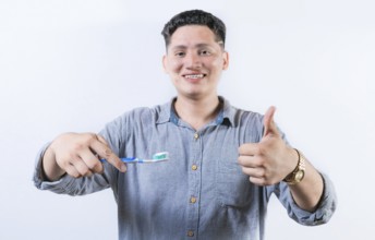 Smiling young man holding a toothbrush gesturing OK. Person holding toothbrush with thumbs up. Guy