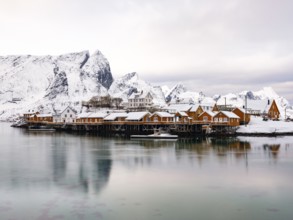 Traditional yellow rorbuer huts on the island of Sakrisøy, snow-covered rocky mountains in the