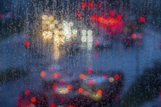 Rainy weather, road traffic, raindrops on a window pane, behind, blurred, lights of vehicles on a