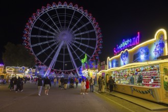 A lively funfair at night with an illuminated Ferris wheel and shops full of people, Cannstatter