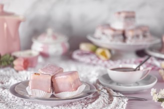 Pink glazed cakes, punch doughnuts and a coffee cup on a table decorated with flowers