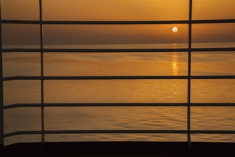 Close-up of silhouetted railing on cruise ship and golden setting sun over Adriatic sea near Zadar,