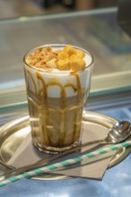 A glass of iced coffee with cream and caramel on a tray, served with a straw and spoon, autumn