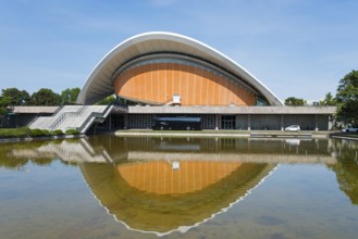 Modern building with curved roof, reflected in the water against a clear sky, House of World