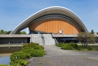 Building with curved roof and wide staircase, surrounded by nature, under a clear sky, House of