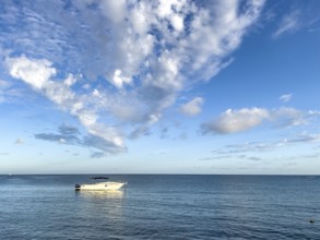 White pleasure craft small motorboat anchored in lagoon bay, white clouds above Cirrocumulus,