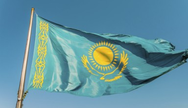 The flag of Kazakhstan flutters in the wind, isolated against a blue sky