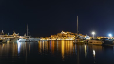 Luxury yachts anchoring in the harbour, behind the illuminated fortress and the old town, night