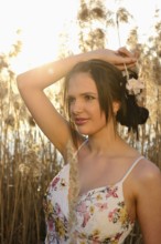 Woman in a floral dress standing in dry reeds, lit by sunlight, Bavaria