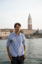 Young man in striped shirt and shorts on the banks of the Grand Canal, behind Campanile, Venice,