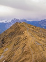 A narrow path winds its way over an autumn-coloured mountain ridge against an alpine backdrop,