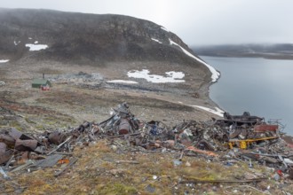 Scrapyard in rocky coastal landscape with snow remains, arctic settlement Ittoqqortoormiit,