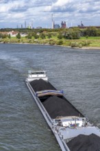 Rhine near Duisburg-Laar, freighter loaded with coal, houses on the dyke road, industrial backdrop