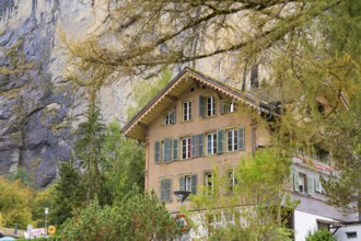 Traditional house in the mountains, surrounded by autumnal trees and a rocky landscape,