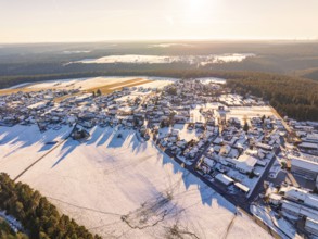 Snowy village in the evening light with extensive fields and neighbouring forest, cast shadows,