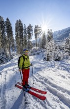 Ski tourer in snowy winter forest with sun star, ascent to Teufelstättkopf, Snowy mountain