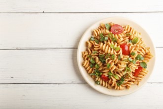 Fusilli pasta with tomato sauce, cherry tomatoes, lettuce and herbs on a white wooden background.