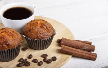 Two carrot muffins with cup of coffee on wooden kitchen board on white wooden background with