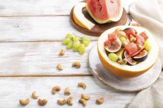 Vegetarian fruit salad of watermelon, grapes, figs, pear, orange, cashew on white wooden background