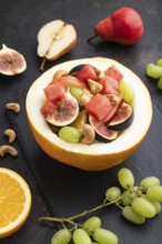 Vegetarian fruit salad of watermelon, grapes, figs, pear, orange, cashew on slate board on a black