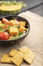 Vegetarian vegetable salad of tomatoes, pumpkin, microgreen pea sprouts on black concrete